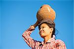 Portrait of Young Asian Burmese traditional female farmer carrying clay pot on head going back home, Bagan, Myanmar