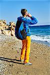 young man standing on the beach against sea and blue sky at early morning and talking by the phone