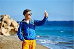 traveler with backpack making selfie against sea and blue sky at early morning