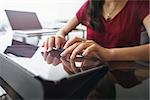 Closeup of hands of female computer technician sitting and typing on tablet computer with laptop in background