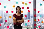 Portrait of proud assistant with pen in mouth. The woman stands in office at high floor, against window full of adhesive notes with tasks