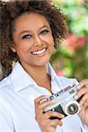 A beautiful mixed race African American girl or young woman outside looking happy taking pictures or photographs with a retro digital camera
