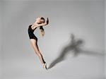 Ballerina in black outfit posing on toes over grey studio background.