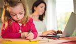 Mother on laptop while daughter drawing at home