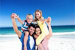 Cute parents giving piggy backs to their children on the beach