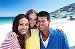 Cute family smiling with arms around on the beach