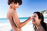 Son putting sunscreen on his mothers nose on the beach