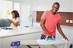 Woman using smartphone while husband using iron in the kitchen