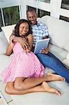 Ethnic couple using tablet lying on the couch in the living room