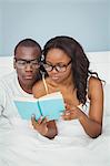 Ethnic couple reading a book in the bed