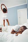 Woman stretching while boyfriend sleeping in the bedroom