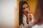 eautiful brunette applyBing lipstick in front of the mirror at home