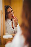 Beautiful brunette applying lipstick in front of the mirror at home