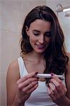 Happy beautiful brunette looking at a pregnancy test in the bathroom at home