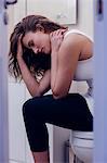 Worried brunette holding her head sitting on toilet in the bathroom