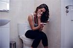 Worried brunette looking at a pregnancy test sitting on toilet in the bathroom