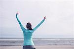 Fit brunette raising her arms at the beach