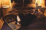 Brunette using laptop lying on the bed at home