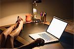 Cropped image of a woman using laptop with feet on the desk at home