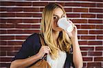 Beautiful woman drinking coffee against brick wall