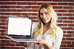 Beautiful blonde woman showing her laptop on brick wall