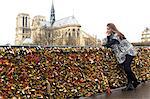 Young woman leaning against love locks, Pont de l'archeveche, Notre Dame Cathedral in background, Paris, France