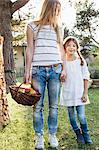 Mother and daughter holding hands, mother holding basket of apples