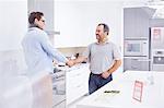 Salesman and young man shaking hands in kitchen showroom