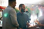 Young men in public house holding beer bottles leaning against counter smiling