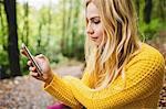 Beautiful blonde woman using smartphone in the woods