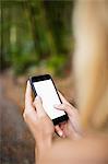 Beautiful blonde woman using smartphone in the woods