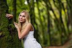 Beautiful blonde woman standing next to a tree trunk in the woods