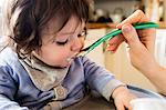 Cute baby being fed by his mother in the kitchen