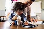 Cute mother showing tablet to her baby in the kitchen