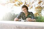 Young man outdoors sitting at table looking down reading book