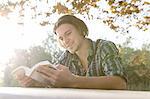 Young man outdoors sitting at table looking down reading book, smiling