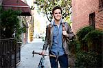 Happy young man strolling with cycle on sidewalk