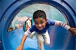 Boy bending forward emerging from playground tunnel