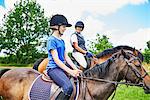 Side view of mature woman and girl on horseback wearing riding hats smiling