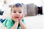 Preschool boy lying on carpet chin in hands, resting on elbows, looking at camera
