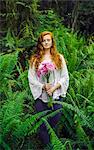 Young woman holding bunch of pink gerberas amongst forest ferns