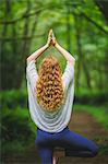 Rear view of young woman in forest practicing yoga in tree pose