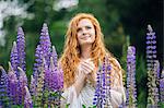Serene young woman amongst purple wildflowers with hands clasped