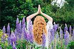 Rear view of young woman meditating with hands together amongst purple wildflowers