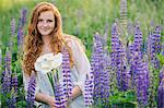 Portrait of young woman amongst purple wildflowers holding bunch of lilies