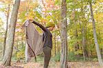 Mid adult woman holding up her shawl in autumn forest