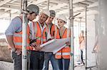 Four female and male builders with blueprint on construction site