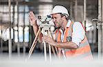 Male surveyor looking through theodolite on construction site