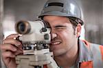Young male surveyor looking through theodolite  on construction site