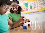 Two young people, boy and girl in a science lesson, wearing eye protectors and working on an experiment.